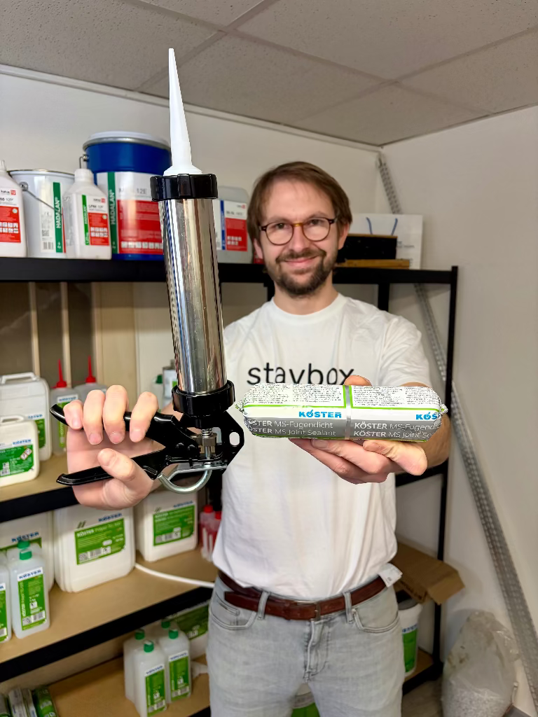 Detailní pohled na menší 310ml balení elastického tmelu KÖSTER MS-Joint Sealant a výtlačnou pistoli připravenou k aplikaci.